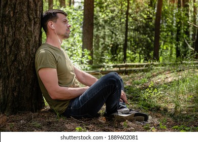 a man in a forest lean against a tree, with headphones listening to music. rest at nature. in the background blurred silhouettes of trees. digital detox. Mental health. Positive emotion. - Powered by Shutterstock