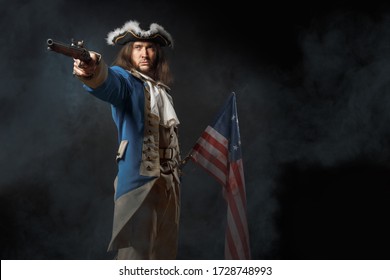 Man In Form Of Officer Of United States Revolutionary War With A Flag And Gun. July 4th, Independence Day USA Concept. Studio Photo On Black Background