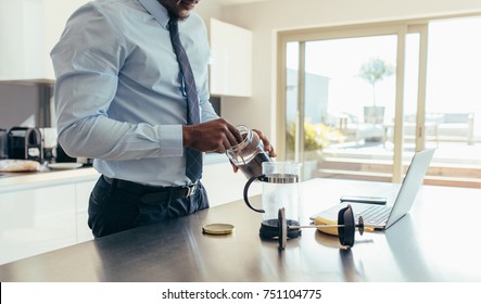 Man in formal clothes making coffee using French press with a laptop computer on kitchen table. Businessman preparing coffee while doing office work at home. - Powered by Shutterstock