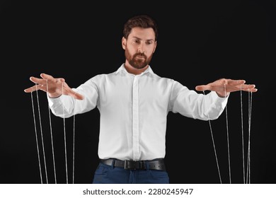 Man in formal outfit pulling strings of puppet on black background, low angle view