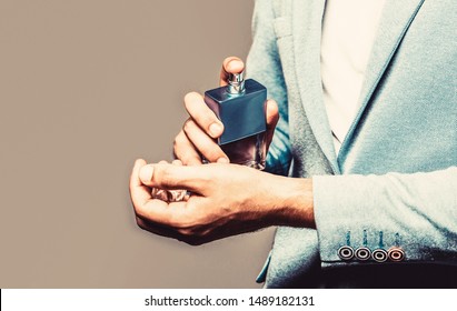 Man In Formal Suit, Bottle Of Perfume, Closeup. Fragrance Smell. Men Perfumes. Fashion Cologne Bottle. Man Holding Up Bottle Of Perfume. Men Perfume In The Hand On Suit Background. Copy Space.