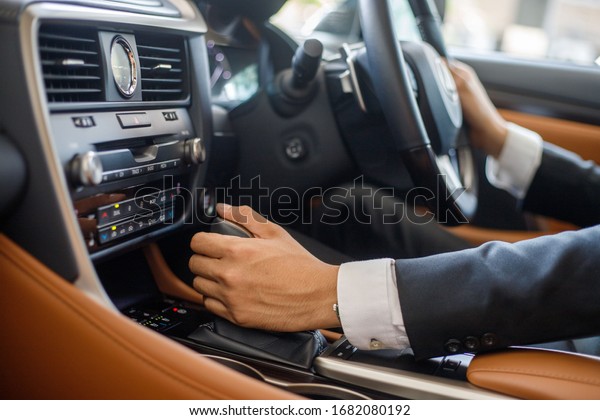 Man in formal suit on driver\'s seat of\
car.close up hand change automatic\
gear.