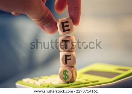 A man forming the acronym ETF for Exchange Traded Fund with wooden dice that are stacked on top of a calculator. A money symbol in the composition.
