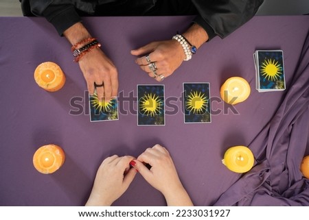 Man fortune teller holding tarot cards in his hands and unrecognizable woman picking the card. Copy space