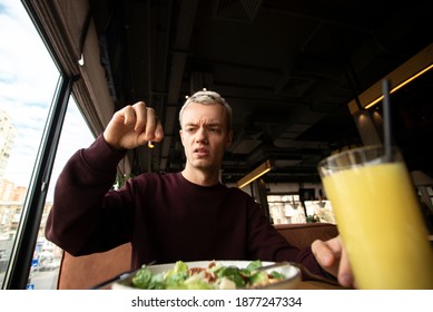 Man Found Something Disgusting In His Meal In The Restaurant. Bad Customer Service Concept. Good Looking Blong Young Man Holds Hair That He Found In A Dish In His Hand And Looks At It With Loathing.