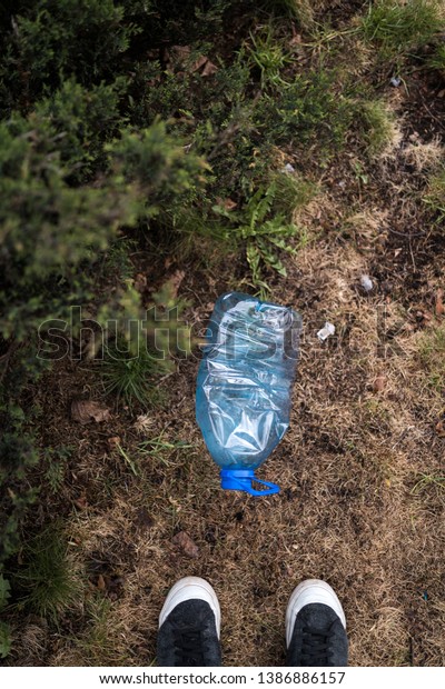 Man\
found standing feet - Blue big plastic bottle lying on the ground\
in tree in a park forest - Thrown out not recycled - Trash and\
pollution of the city and nature - Decayed\
rubbish