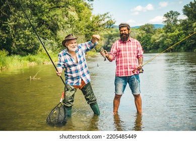 Man Friends. Two Men Friends Fishing. Flyfishing Angler Makes Cast, Standing In River Water. Old And Young Fisherman.