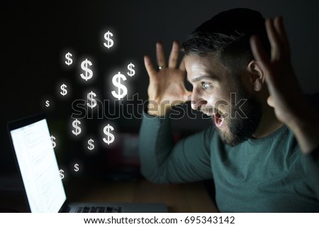 Man in front of the computer with raised hands get paid. Business and money concept. Dollars flying.