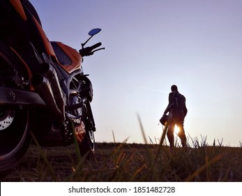 Man in a full leather suit with his motorbike during sunset