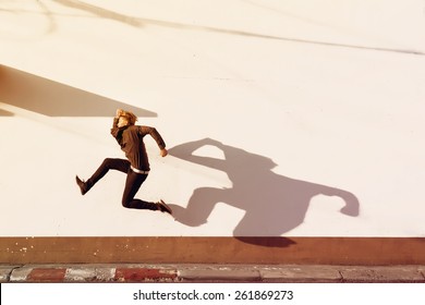 Man With Funny Long Shadow Jumps On Background Of White Wall. Place For Text