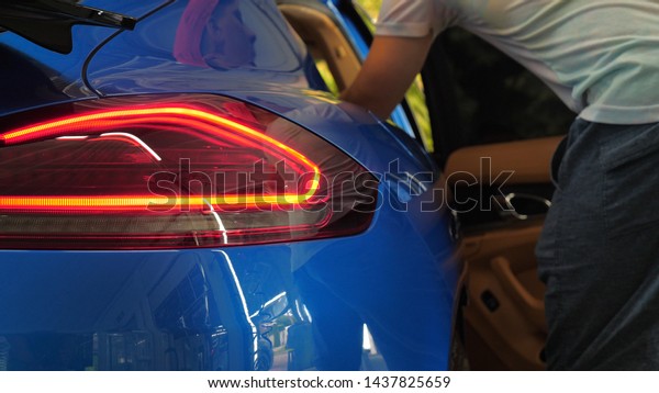 A man in the garage (Service) salon puts his bag in\
the salon (in the trunk), checking and turning off the car alarm. A\
man opens the door and trunk in a new car. Concept of: Slow mo, Car\
shop, Man.