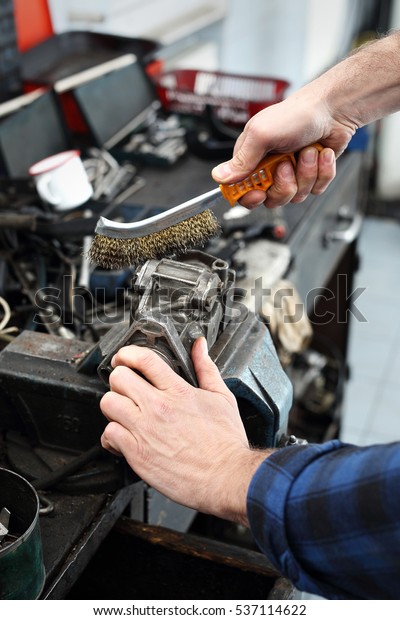 The man in the garage with a wire brush cleans\
mechanical parts 