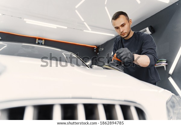 Man in a garage. Worker polish a car. Man in a\
black uniform.