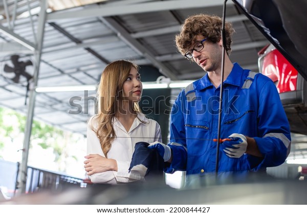 Man garage worker and woman customer talking to\
discuss the details of car repairs. male mechanic check engine oil\
and recommend use for female client. Transportation and car\
insurance concept.