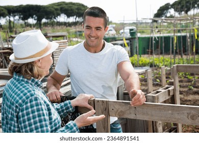 Man gardener talking with grandmother near wooden fence in garden outdoor - Shutterstock ID 2364891541