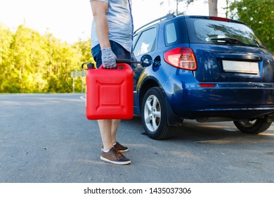 Man with a gas can on the side of the road with his car in background, close-up without a face. Driver with refuel canister of fuel on background of stalled car . Concept of empty fuel tank - Powered by Shutterstock