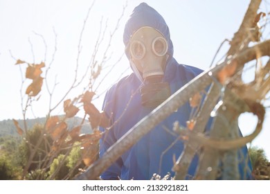 Man With Gas Mask With Filter And Blue Suit Hiding Behind Some Branches. Concept Of Chemical Warfare. Copy Space