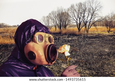Man in the gas mask holding a flower. Radiation influence. Environmental pollution. Dangerous nuclear power. Ecological disaster.Nature is on fire. Burnt forests. Empty field.