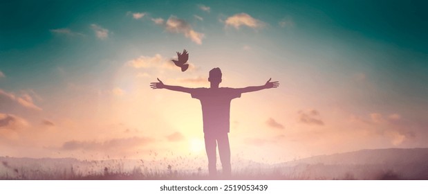 A man gazes skyward, his arms open, embracing the freedom as his silhouette blends with the sunset sky, a bird soaring above the serene landscape, bathed in the light of dusk, scenic beauty of nature. - Powered by Shutterstock