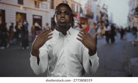 Man gesturing with hands and touching temple on a busy city street, wearing white shirt and glasses; passionate speech.