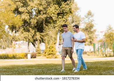 Man Gesturing While Walking And Talking With Teenager Son In Park