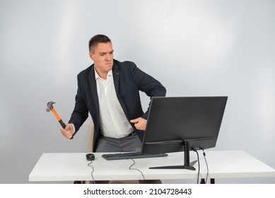 The Man Gets Angry And Smashes The Monitor With A Hammer. An Office Worker In A Rage Breaks The Computer. 