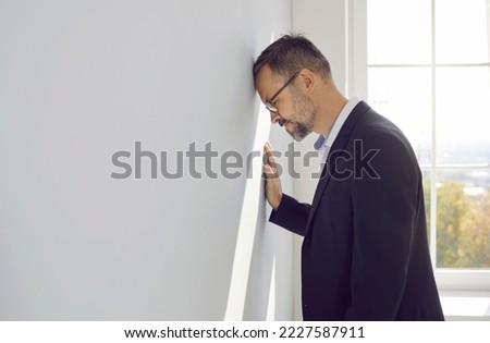 Man gets bankrupt, loses business, feels overworked defeated frustrated unsuccessful hopeless disappointed tired of stress, finance economy problems, debts, bangs head against light gray office wall