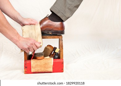 A Man Gets His Shoes Polished By A Worker Using A Vintage Shoe Shine Box With Camel Hair Brushes, Polishing Rag, Polish And A Wooden Shoe Platform.