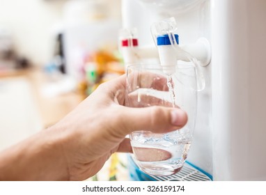 Man getting a cold, refreshing drink from the water cooler. - Shutterstock ID 326159174