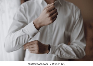 A man is getting dressed in a white shirt and is adjusting his shirt sleeves. Concept of formality and attention to detail, as the man is taking the time to properly dress himself - Powered by Shutterstock