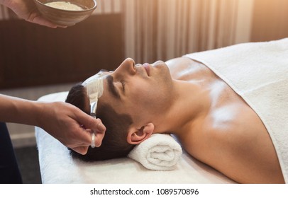 Man Getting Facial Nourishing Mask By Beautician At Spa Salon, Closeup. Apply Face Mask, Spa Beauty Treatment And Skincare.