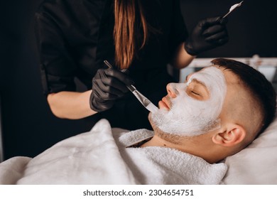 Man getting facial nourishing mask by beautician at spa salon, closeup. Apply face mask, spa beauty treatment and skincare. - Powered by Shutterstock