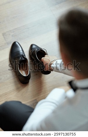A man is getting ready for a formal event, putting on his shoes and adjusting his tie. Concept of preparation and attention to detail, as the man takes the time to ensure his appearance is polished