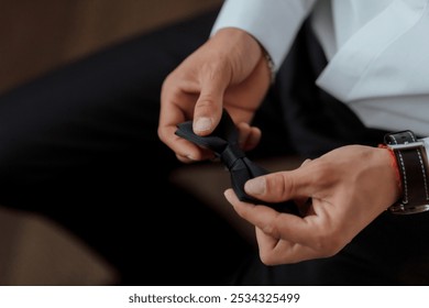 A man is getting ready to tie his tie. He is wearing a black suit and white shirt - Powered by Shutterstock