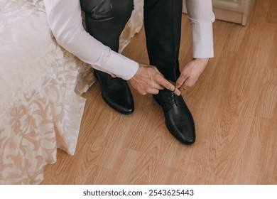 A man is getting ready for a wedding and is adjusting his shoes. Concept of formality and elegance, as the man is dressed in a suit and tie - Powered by Shutterstock