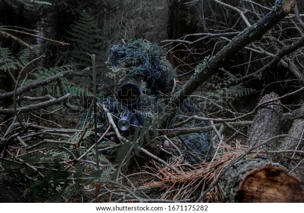 Man in\
a ghillie suit hidden in the forrest, aiming through a scope on a\
rifle. May both represent a sniper or a hunter.\
