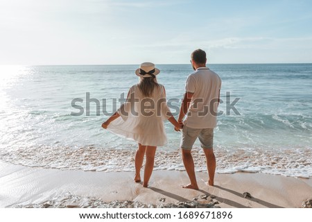 man and a girl hold hands and watch the sunset on the beach