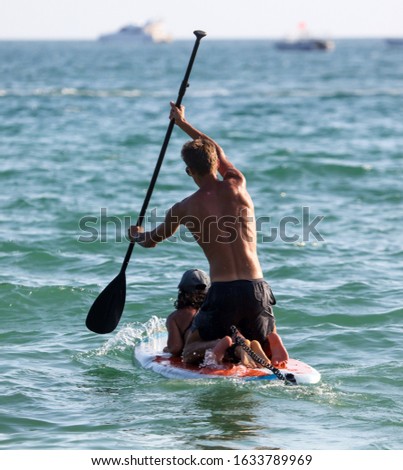 A man and a girl swim in the sea on a surfer.