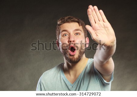 Man give stop hand sign gesture. Facial expression open mouth black background.