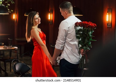 Man Gives Flowers. Romantic Couple Have Dinner In The Restaurant.