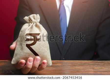 Man gives a Indian rupee money bag. Loan issuance. Financial support, leasing. Investments, financing Lobbying. Funding. Accounting, tax payment. Earnings and profits.