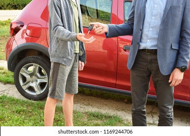 Man Gives Keys Of Red Car To Teenage Boy For Learning To Drive Or Taking Driving Test. Father And Son Family Time Concept.
