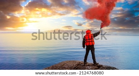 Man gives SOS signal. Person on seashore blows red smoke. Concept of distress and search for help. Human in orange vest is signaling for help. Man with flue on sea shore. Metaphor for need for support