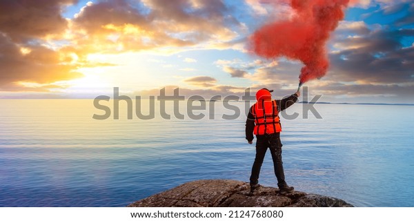 Man gives SOS signal. Person on seashore blows\
red smoke. Concept of distress and search for help. Human in orange\
vest is signaling for help. Man with flue on sea shore. Metaphor\
for need for support
