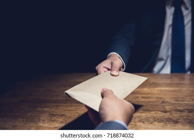 A man giving bribe money in a brown envelope to another businessman in a corruption scam - Shutterstock ID 718874032