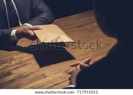 A man giving bribe money in a brown envelope to another businessman in a corruption scam
