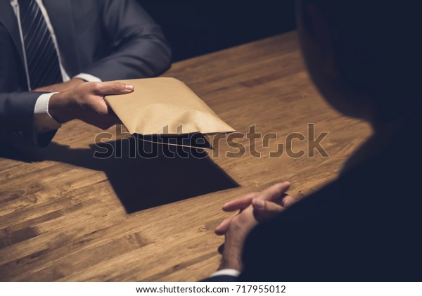 A man giving bribe money in a brown\
envelope to another businessman in a corruption\
scam