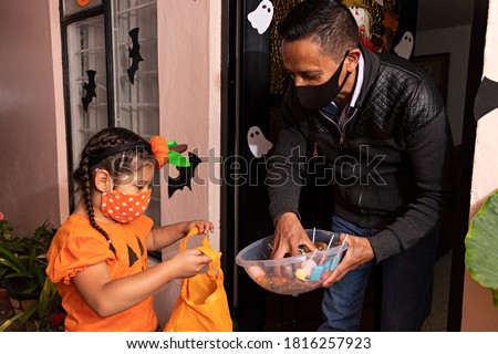 A man giving candies to a girl dressed in a pumpkin costume in the night of halloween