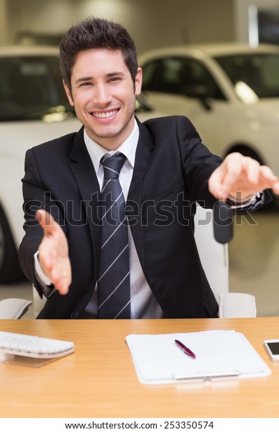 Man giving a customer keys while reaching for\
handshake at new car\
showroom