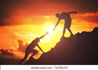 Man is giving helping hand. Silhouettes of people climbing on mountain at sunset. - Shutterstock ID 712781473